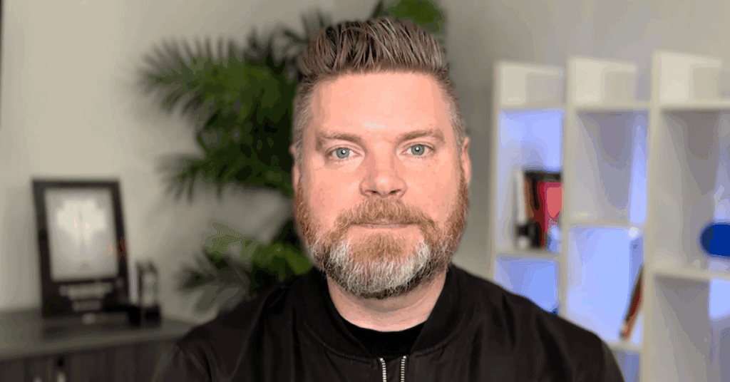 Andrew Aebersold, CEO of Mediaura, looks into the camera while explaining how the latest Google algorithm update has changed SEO for the healthcare industry. He is wearing a black zip up. The background is an office scene, featuring a bookshelf and plant.