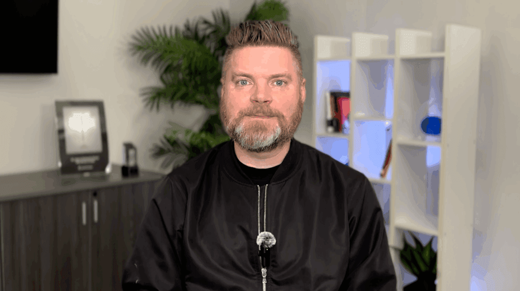 Andrew Aebersold, CEO of Mediaura, looks into the camera while explaining the importance of audience targeting and digital marketing and the most important groups to target. He is wearing a black zip up. The background is an office scene, featuring a bookshelf and plant.