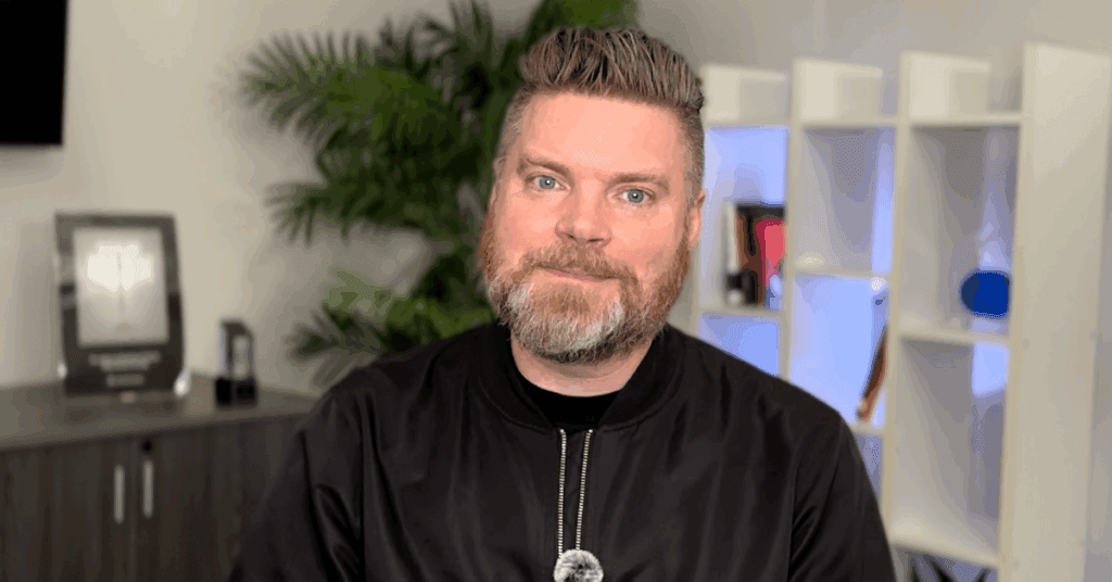 Andrew Aebersold, CEO of Mediaura, looks into the camera while explaining marketing mistake of not monitoring ad campaigns close enough. He is wearing a black zip up. The background is an office scene, featuring a bookshelf and plant.